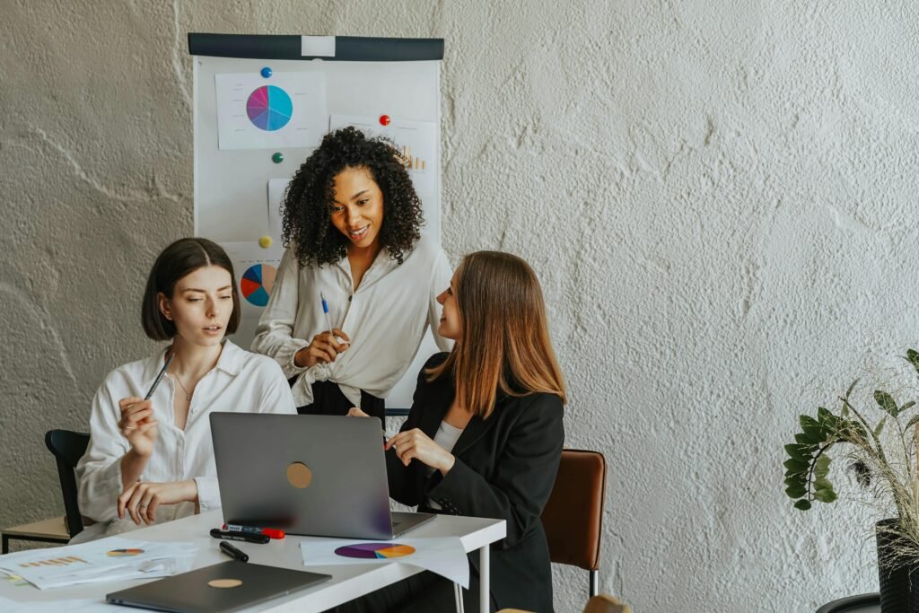 Three colleagues collaboratively working on a project in an office setting with charts and laptops.